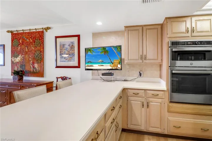 Kitchen with double oven, backsplash, light brown cabinetry, and light hardwood / wood-style flooring