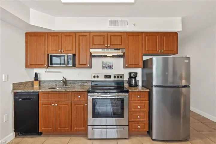 Kitchen with dark stone countertops, sink, stainless steel appliances, and light tile patterned flooring