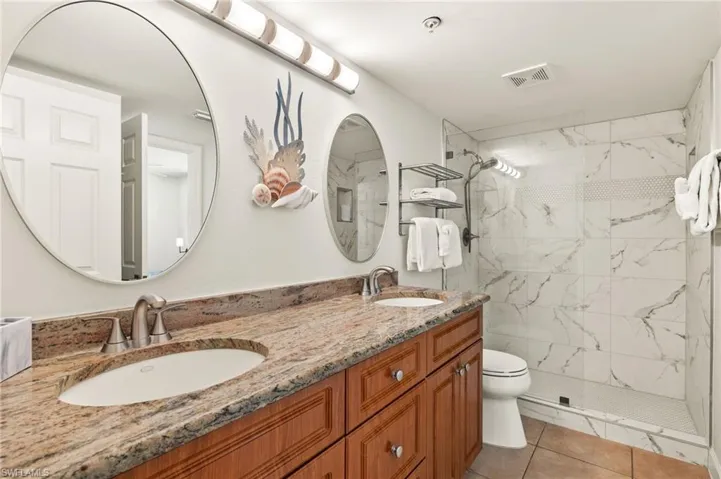 Bathroom with a tile shower, vanity, tile patterned floors, and toilet