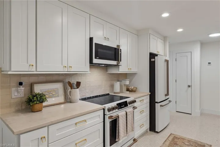 Kitchen with premium appliances, white cabinetry, light stone countertops, and tasteful backsplash