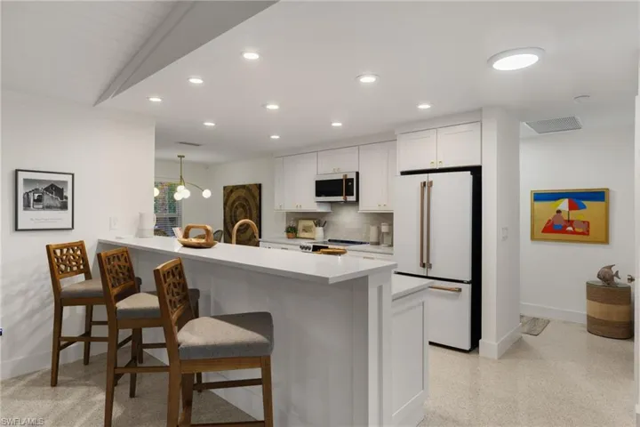 Kitchen featuring kitchen peninsula, white fridge, a kitchen bar, white cabinetry, and vaulted ceiling