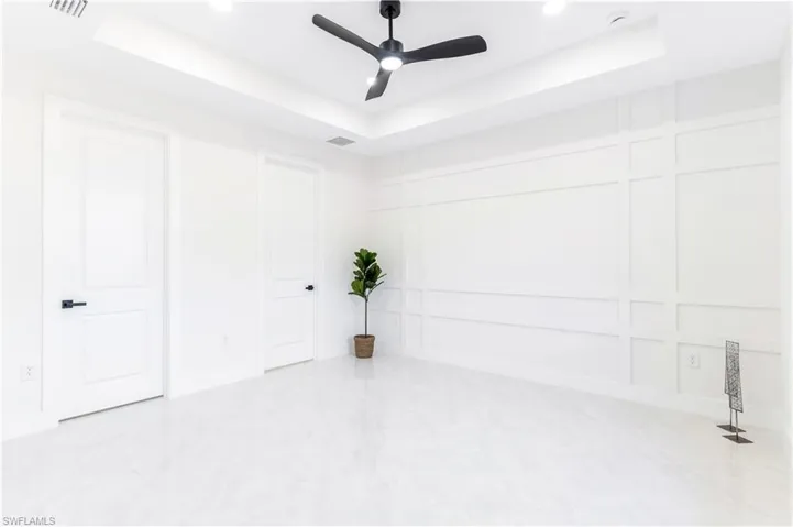 Empty room featuring a raised ceiling, ceiling fan, and a decorative wall