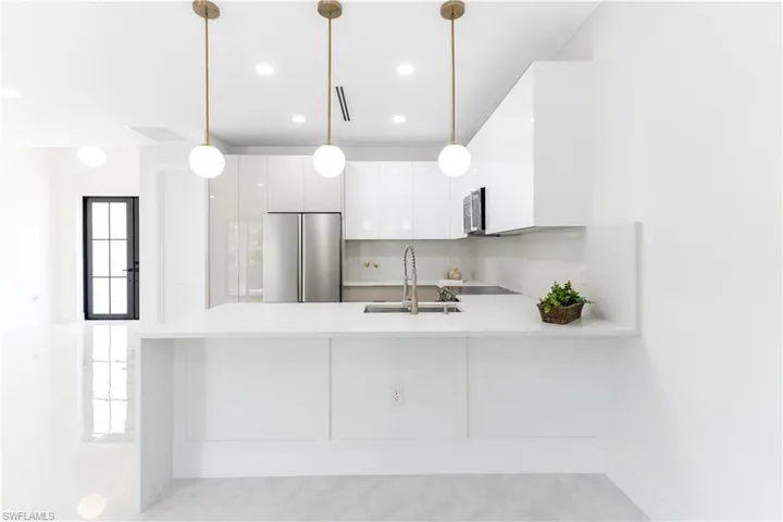 Kitchen with white cabinets, a peninsula, modern cabinets, stainless steel appliances, and decorative light fixtures