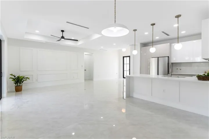 Living room with a raised ceiling, a decorative wall, a ceiling fan, and recessed lighting