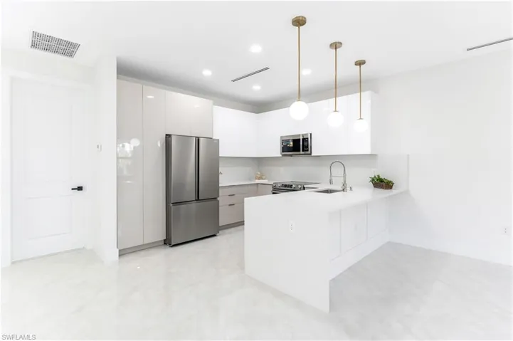 Kitchen featuring stainless steel appliances, a peninsula, hanging light fixtures, modern cabinets, and white cabinetry