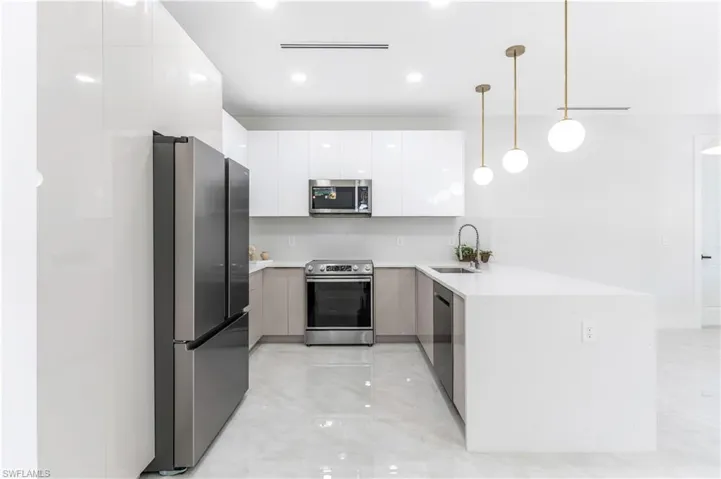 Kitchen with a peninsula, stainless steel appliances, modern cabinets, hanging light fixtures, and white cabinets