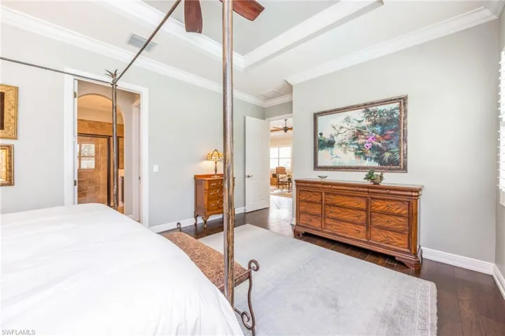 Bedroom featuring crown molding, a tray ceiling, ceiling fan, dark hardwood / wood-style floors, and a closet