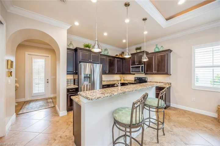 Kitchen with decorative light fixtures, dark brown cabinets, light stone countertops, appliances with stainless steel finishes, and light tile patterned floors