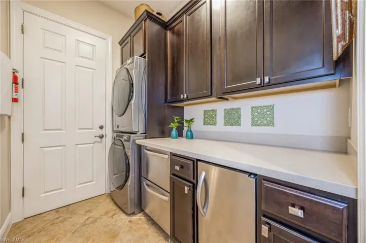 Laundry room with cabinets, stacked washer and dryer, and light tile patterned floors