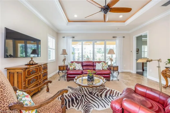 Tiled living room featuring ceiling fan, a tray ceiling, and ornamental molding