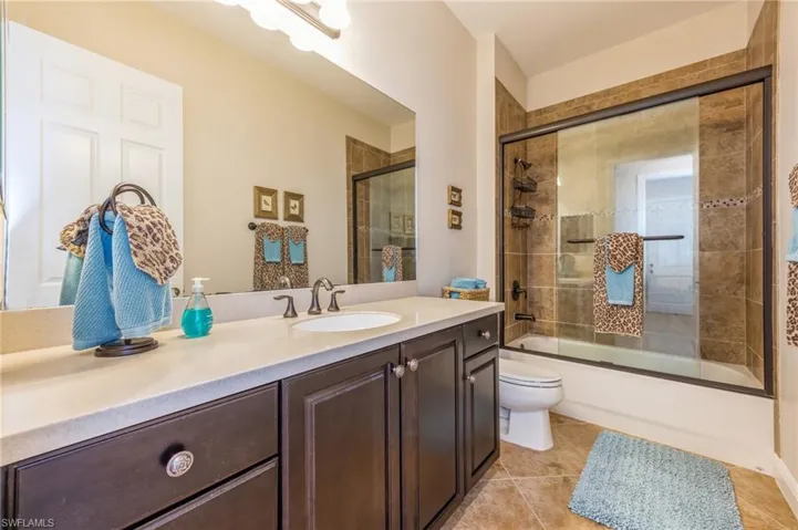 Full bathroom with vanity, toilet, bath / shower combo with glass door, and tile patterned flooring