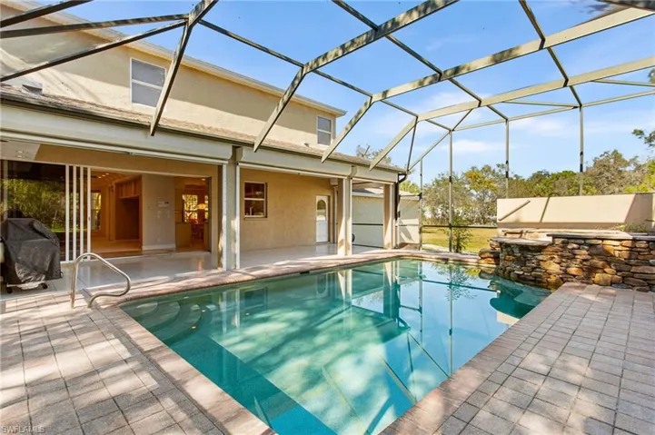 Screened enclosure housing a rectangular swimming pool with integrated spa featuring a stacked stone surround
