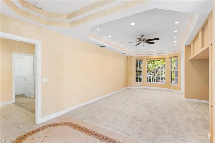 Spacious room featuring a tray ceiling with recessed lighting and a ceiling fan, a bay window, and light-toned carpeting