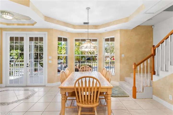 Tile flooring with decorative inlay, French doors, multiple windows, tray ceiling, and a staircase with wood railing