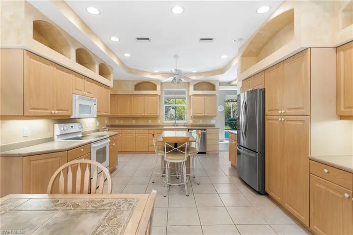 Spacious kitchen featuring extensive light wood-finish cabinetry, neutral-toned tile flooring, recessed lighting, and a stainless steel refrigerator
