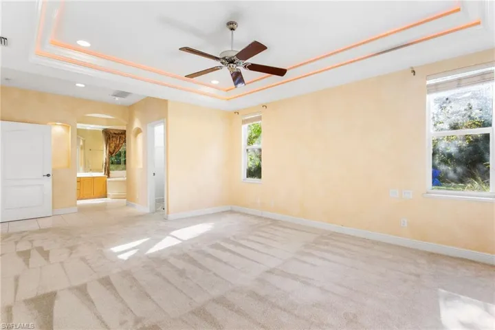 Recessed ceiling with integrated lighting, centered ceiling fan, and light beige carpet flooring