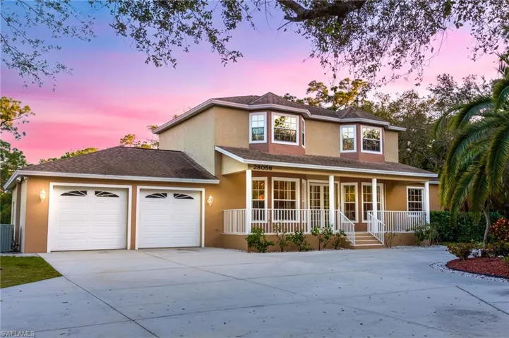 Two-story residence featuring stucco exterior, a covered front porch with white railings, and a two-car garage with individual doors