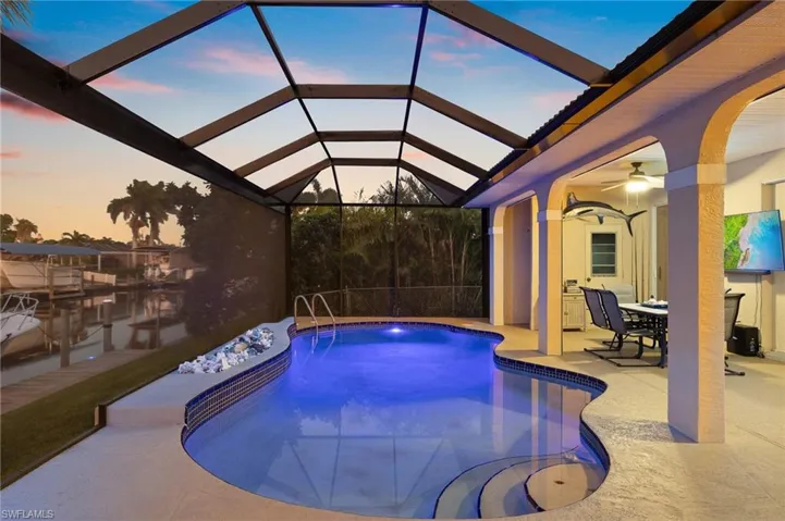 Pool at dusk featuring an outdoor pool, glass enclosure, a sunroom, and a ceiling fan