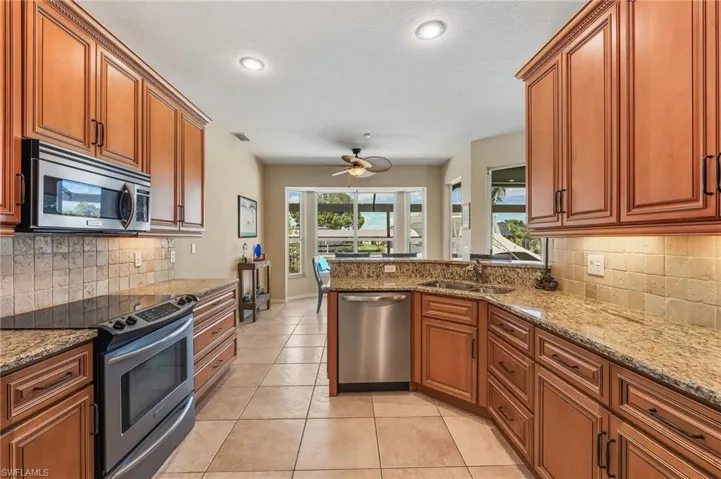 Kitchen featuring decorative backsplash, stainless steel appliances, brown cabinets, light stone counters, and recessed lighting