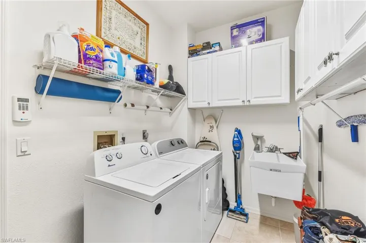 Laundry area with cabinet space, light tile patterned floors, and washer and clothes dryer