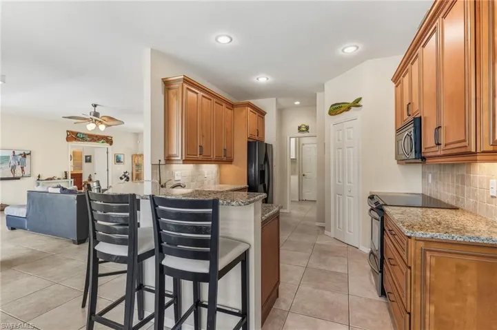Kitchen featuring brown cabinets, black appliances, tasteful backsplash, a breakfast bar, and ceiling fan
