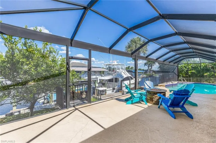 Swimming pool featuring glass enclosure, a sunroom, an outdoor fire pit, a patio area, and a water view