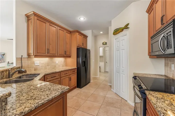 Kitchen featuring decorative backsplash, brown cabinets, black refrigerator with ice dispenser, stainless steel microwave, and recessed lighting