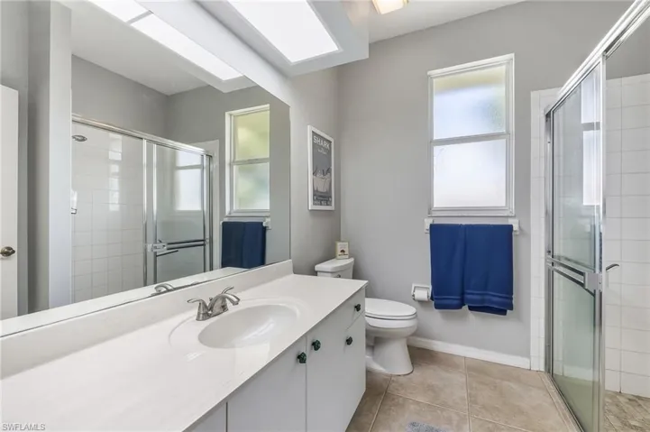 Full bath featuring light tile patterned floors, vanity, a stall shower, and a skylight