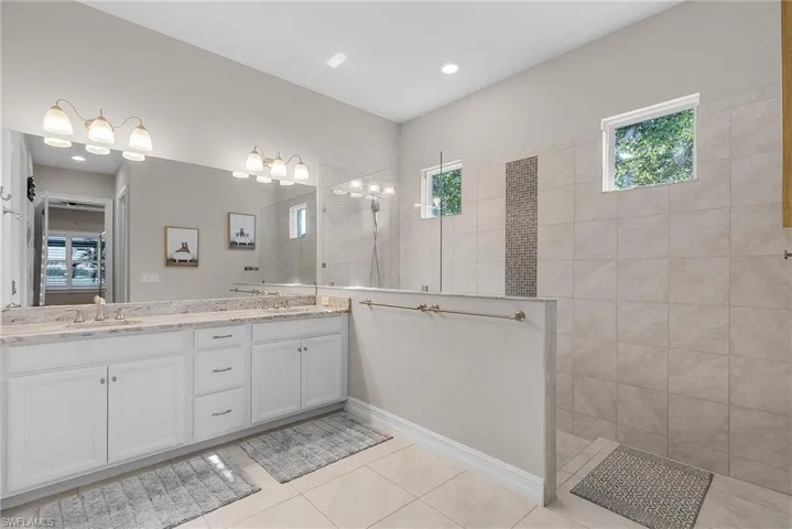 Primary bathroom featuring healthy amount of natural light, double vanity, walk in shower, and light tile patterned flooring