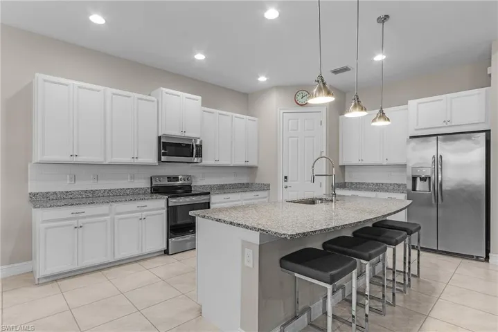 Kitchen with stainless steel appliances, a breakfast bar area, hanging light fixtures, white cabinetry, and light tile patterned floors