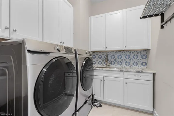 First floor laundry area with washer and dryer, light tile patterned floors, and cabinet space