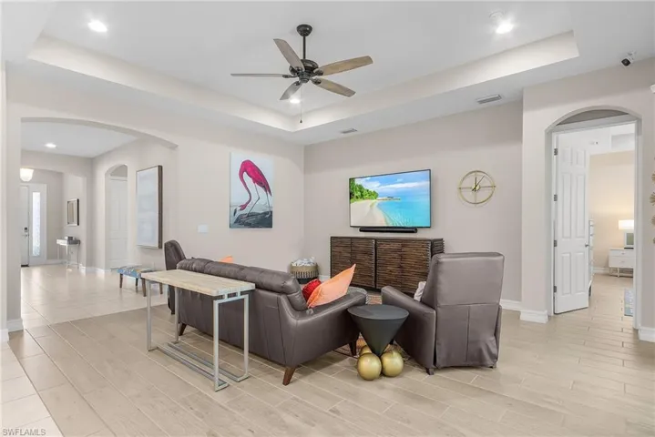 Living room featuring arched walkways, a raised ceiling, a ceiling fan, recessed lighting, and wood finish floors