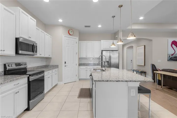 Kitchen featuring appliances with stainless steel finishes, white cabinetry, light stone counters, arched walkways, and hanging light fixtures