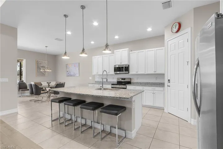 Kitchen with appliances with stainless steel finishes, an island with sink, pendant lighting, light stone counters, and a breakfast bar area
