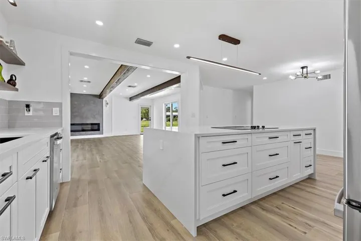 Kitchen with white cabinets, hanging light fixtures, light hardwood / wood-style flooring, a kitchen island, and stainless steel dishwasher