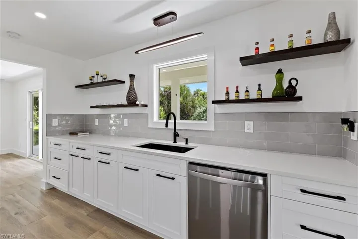 Kitchen with backsplash, light hardwood / wood-style floors, stainless steel dishwasher, sink, and white cabinets