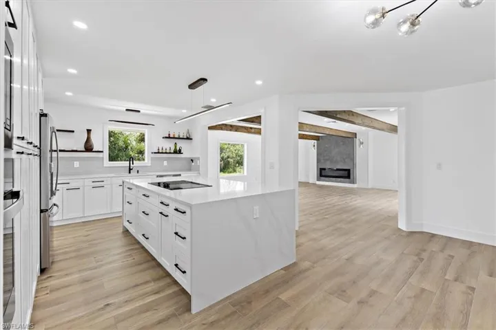 Kitchen featuring black electric stovetop, decorative light fixtures, light wood-type flooring, and white cabinetry