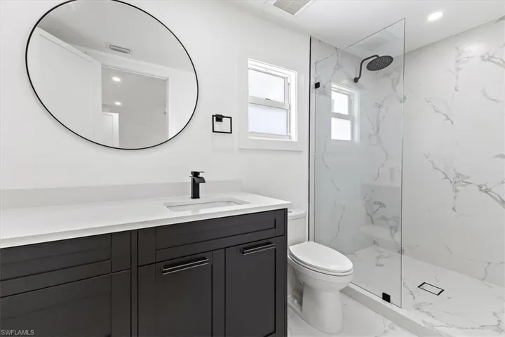 Bathroom with tiled shower, vanity, and toilet
