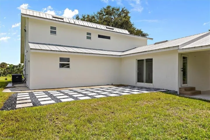 Back of house with central AC, a lawn, and a patio area