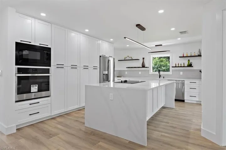 Kitchen featuring black appliances, a center island, light wood-type flooring, and white cabinetry