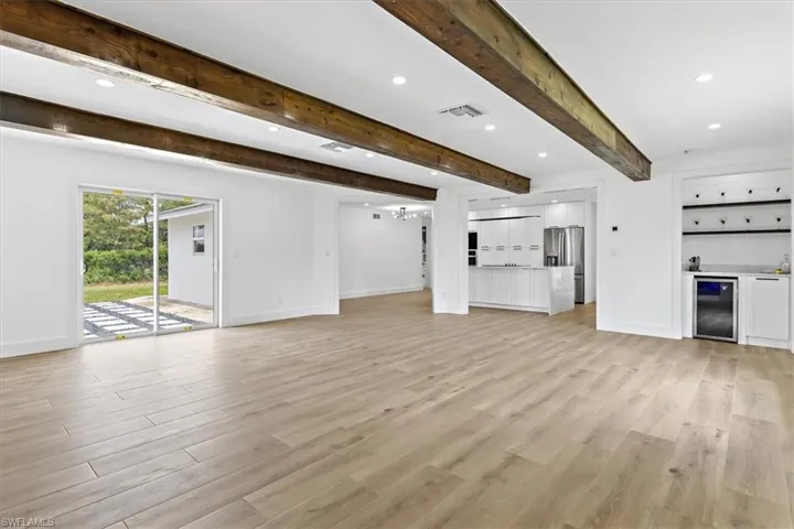 Unfurnished living room with beverage cooler, beamed ceiling, and light hardwood / wood-style flooring