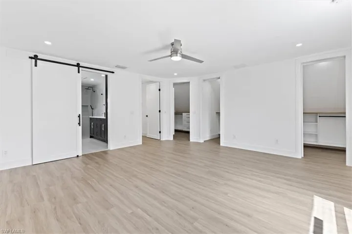Unfurnished bedroom with light wood-type flooring, connected bathroom, ceiling fan, and a barn door