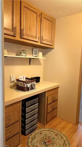 Built-in desk area can be used for a variety of purposes and features wood cabinetry, a light-colored countertop, overhead storage, and wood-like flooring.