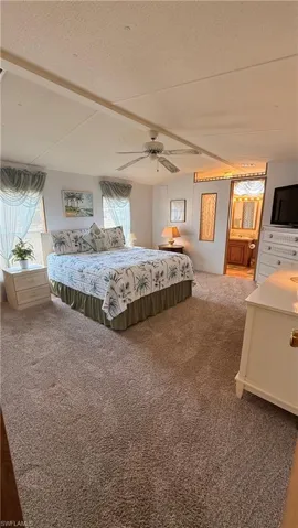 Carpeted primary retreat featuring a ceiling fan on vaulted ceiling, multiple windows with valances & blinds.