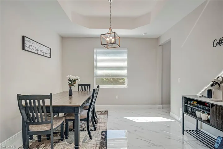 Dining area with light marble finish flooring, a raised ceiling, and hanging lights