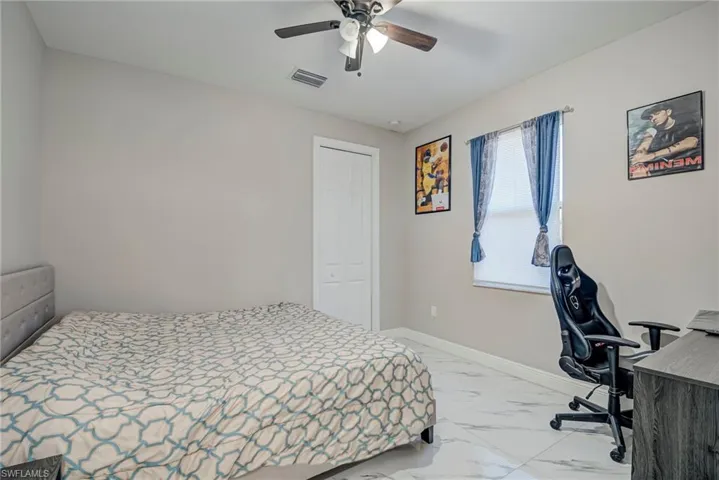 Bedroom featuring an office area, light marble finish floors, a closet, and ceiling fan
