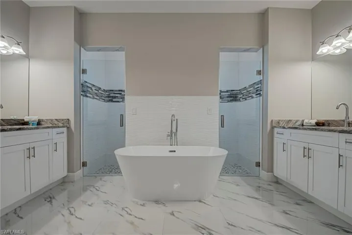 Full bath with two vanities, a shower stall, a soaking tub, and light marble finish floors