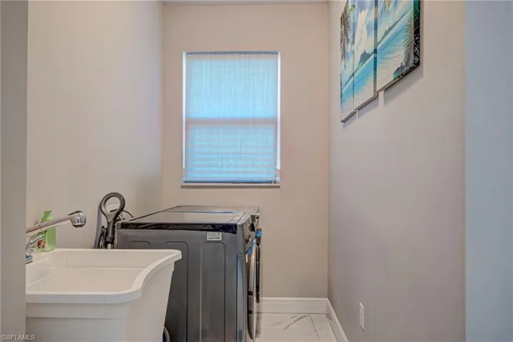 Laundry area with light marble finish floors and washer and clothes dryer