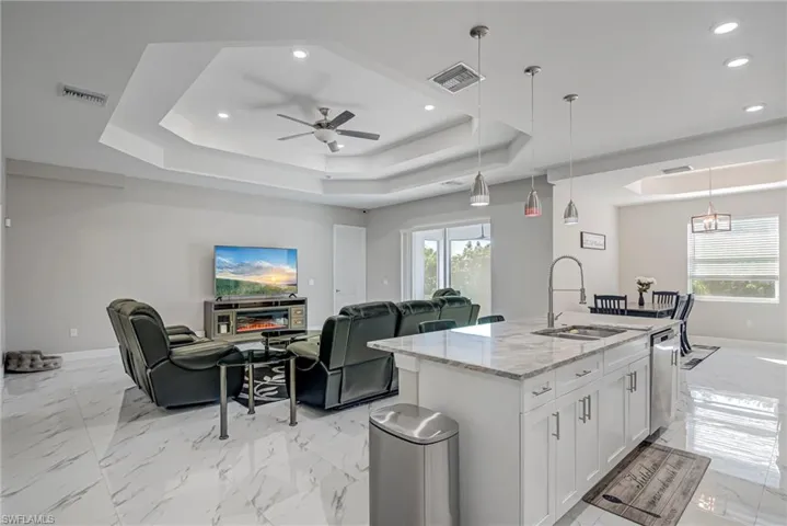 Kitchen with light stone counters, light marble finish floors, white cabinets, pendant lighting, and a center island with sink
