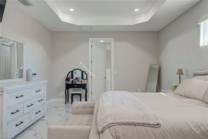 Bedroom featuring a tray ceiling, recessed lighting, and light marble finish floors